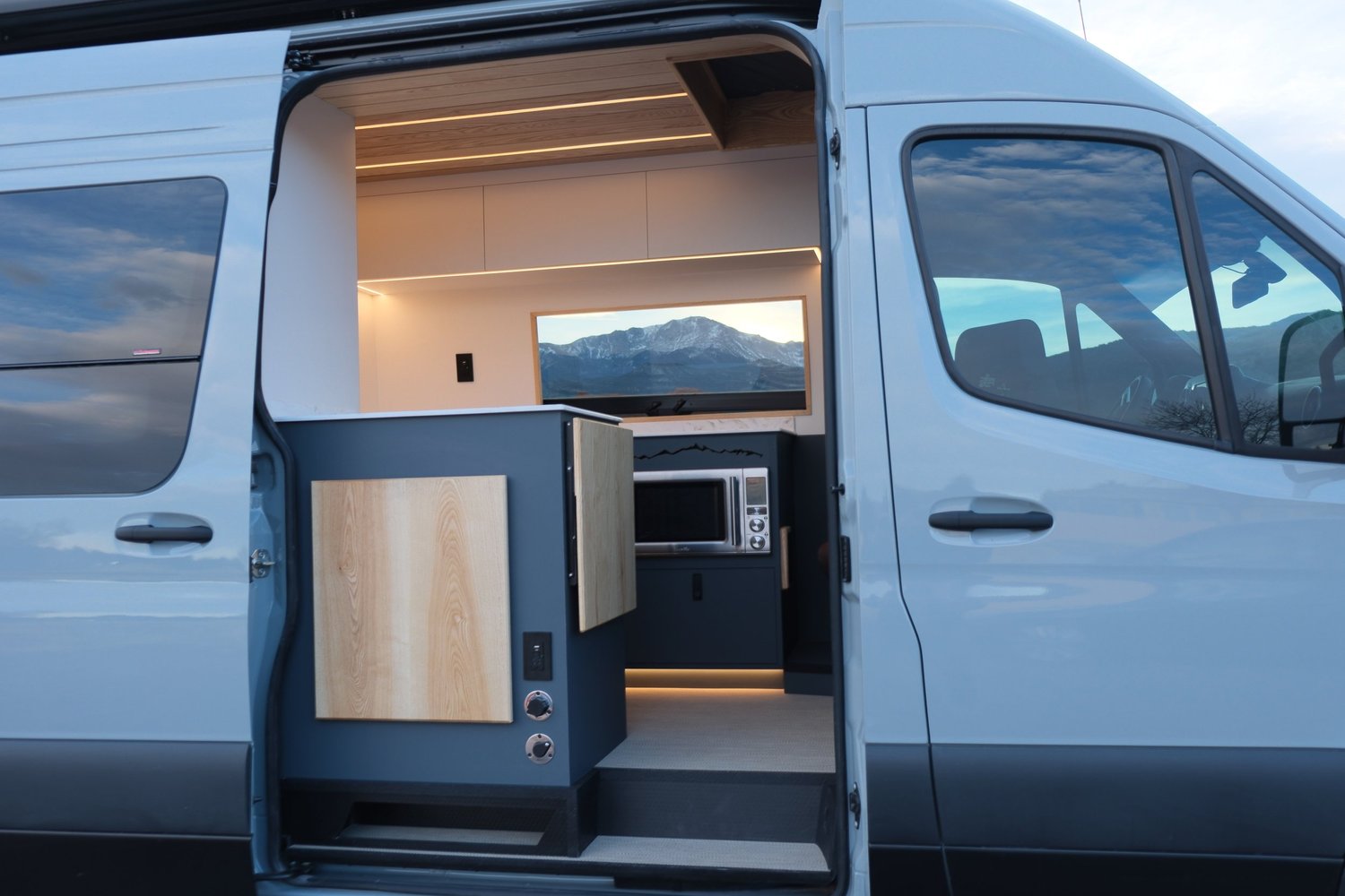 Looking through Midnight’s open side door into the finished kitchen, with illuminated cabinetry and mountain views