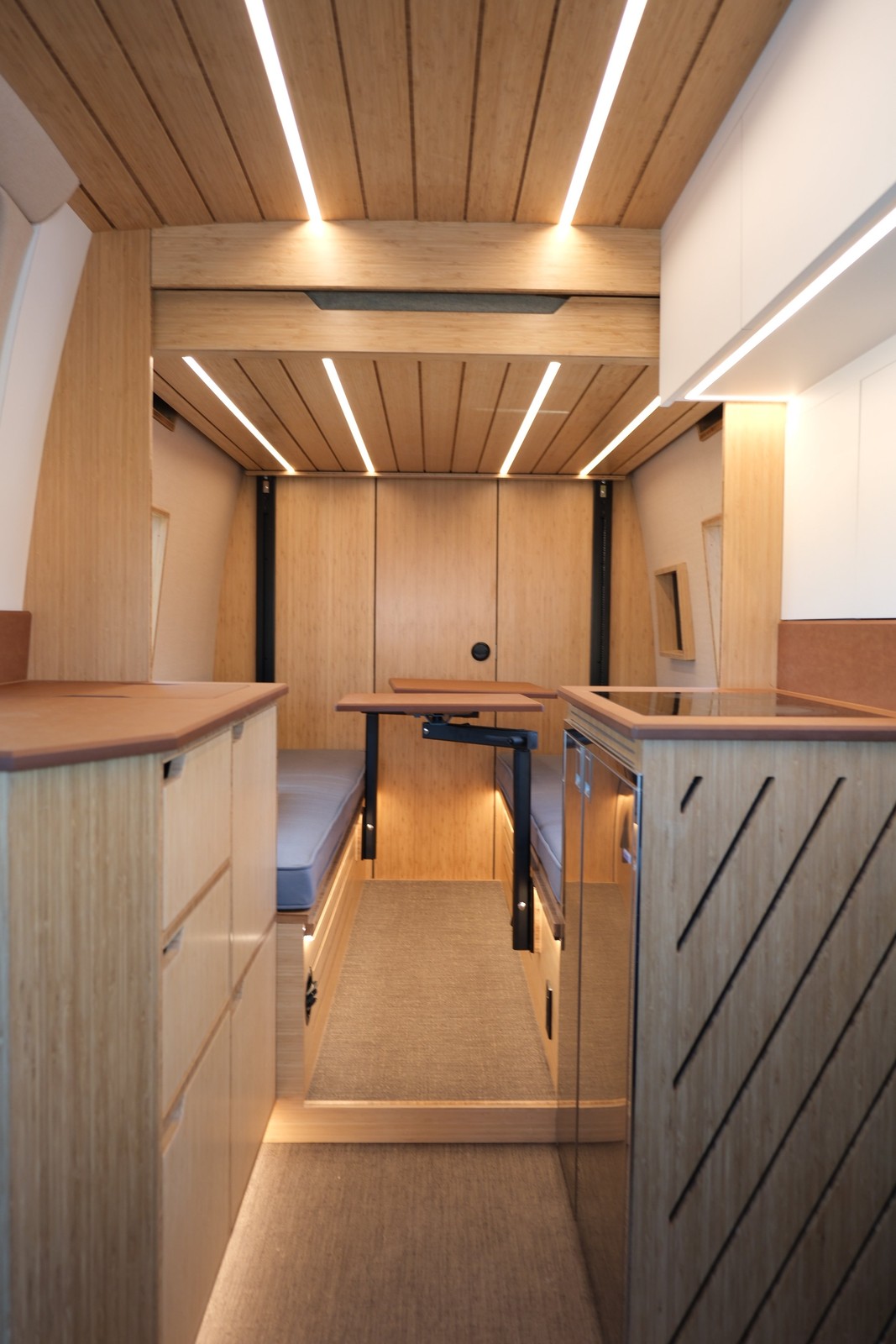 View through the Den galley toward the rear lounge beneath illuminated wood ceiling slats.
