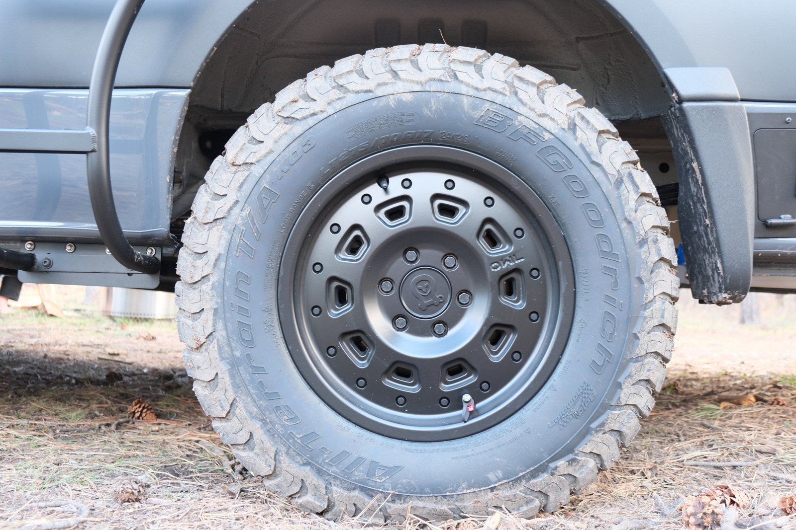 The Den all-terrain tire and dark wheel beside the side step.