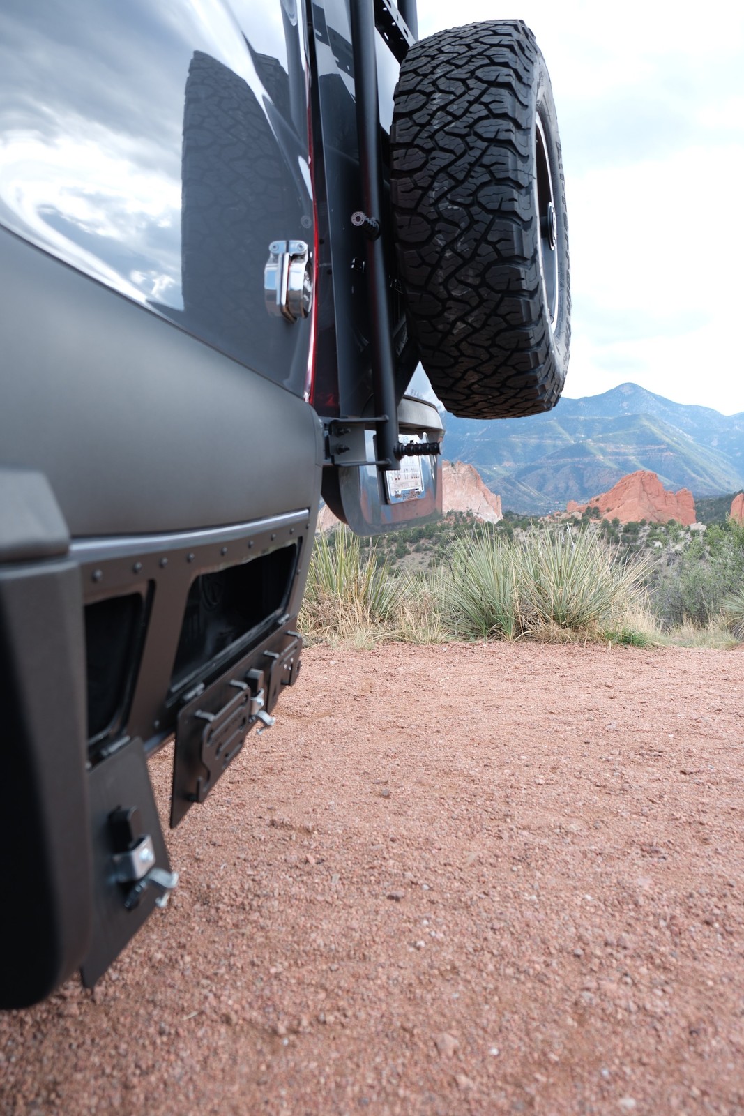 The Den rear bumper and rear-mounted spare tire beside a mountain landscape.