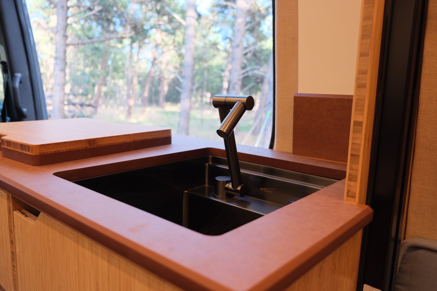 The Den galley sink and black faucet beside a window looking into the woods.