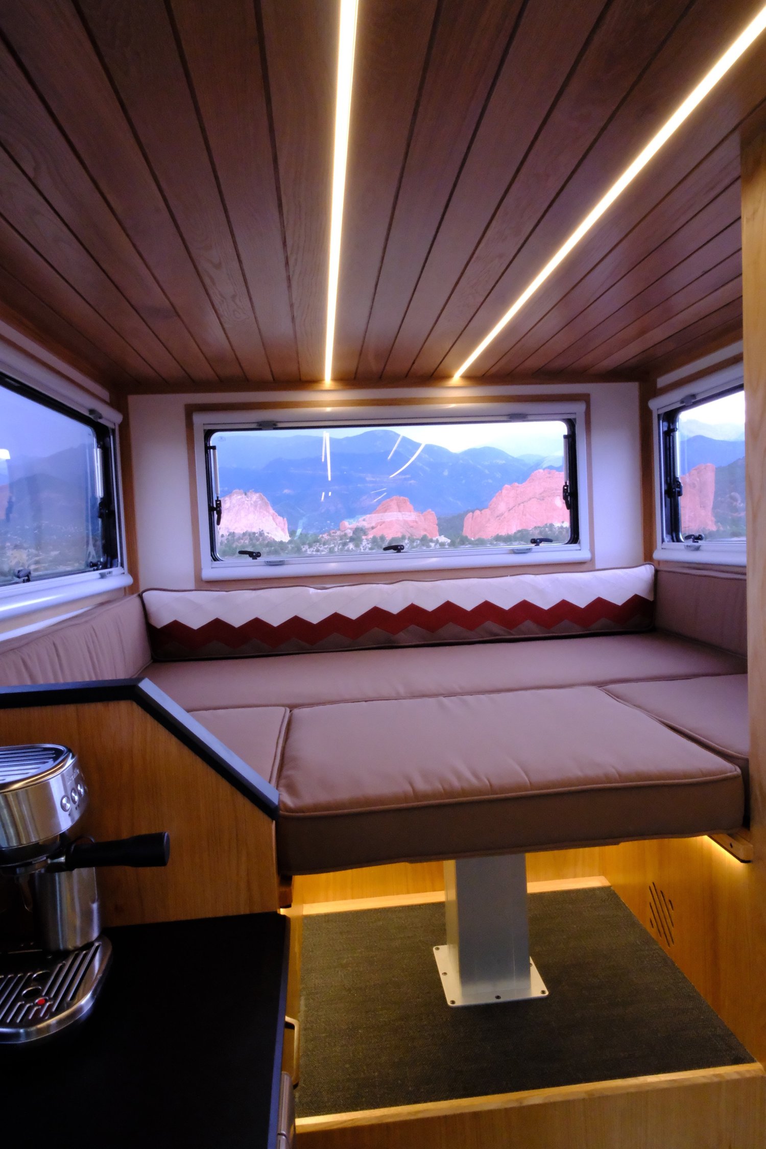 The Nest rear dinette converted to a bed beneath panoramic windows.
